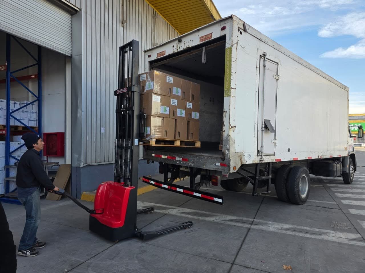 Operario cargando un pallet de cajas a un camión de caja cerrada con apilador eléctrico